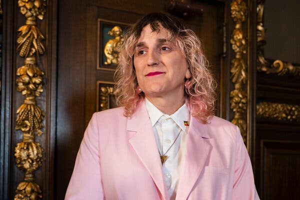 Leigh Finke wearing a pink blazer in front of an ornamental wooden door.